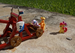 Size: 1519x1082 | Tagged: safe, apple bloom, applejack, g4, blind bag, catapult, cowtapult, irl, outdoors, photo, tiarabuse, tied up, toy