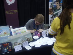 Size: 2048x1536 | Tagged: safe, applejack, rainbow dash, rarity, cat, human, g4, barely pony related, booth, convention, glasses, irl, irl human, katie cook, phoenix comicon, phoenix comicon 2013, photo