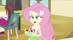 Size: 799x436 | Tagged: safe, screencap, fluttershy, velvet sky, equestria girls, g4, my little pony equestria girls, apple, background human, bowl, cherry, cross-eyed, eyeshadow, female, food, frown, fruit salad, grapes, hair ornament, lidded eyes, makeup, open mouth, orange, salad, solo focus