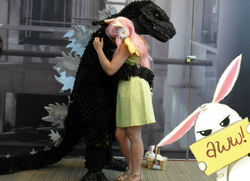 Size: 680x493 | Tagged: safe, angel bunny, fluttershy, kaiju, g4, clothes, cosplay, costume, crossover, dress, glare, godzilla, godzilla (series), hug, looking at you