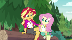 Size: 1280x720 | Tagged: safe, screencap, fluttershy, sunset shimmer, equestria girls, g4, my little pony equestria girls: legend of everfree, camp everfree outfits, clothes, embrace the magic, female, log, mama sunset, motherly, open mouth, scenery, singing, sitting