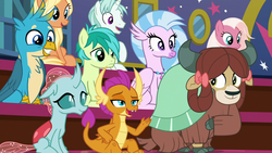 Size: 1280x720 | Tagged: safe, screencap, gallus, ocellus, sandbar, silverstream, smolder, yona, changedling, changeling, classical hippogriff, dragon, earth pony, griffon, hippogriff, pony, unicorn, yak, a rockhoof and a hard place, g4, beak, blanket, bow, chest fluff, claws, cloven hooves, dragoness, fangs, female, floppy ears, hair bow, hair ribbon, horn, jewelry, male, mare, monkey swings, necklace, open mouth, raised hoof, sitting, smiling, stallion, student six, teenager, wings