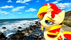 Size: 1200x676 | Tagged: safe, artist:nekokevin, sunset shimmer, pony, unicorn, g4, female, irl, mare, ocean, photo, plushie, rock, smiling, smug, solo