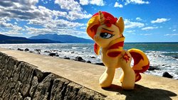 Size: 1200x675 | Tagged: safe, artist:nekokevin, sunset shimmer, pony, unicorn, g4, cloud, female, irl, mare, ocean, photo, plushie, rock, smiling, smug, solo