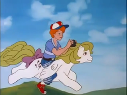 Size: 771x577 | Tagged: safe, screencap, danny williams, surprise, human, pegasus, pony, g1, my little pony 'n friends, the great rainbow caper, adoraprise, baseball cap, belt, bow, camera, cap, clothes, cute, danny riding surprise, duo, female, flying, hat, humans riding ponies, male, mare, pants, ponyland, riding, riding a pony, shirt, shoes, sky, smiling, surprise can fly, t-shirt, tail bow