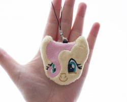 Size: 1000x803 | Tagged: safe, artist:meplushyou, fluttershy, human, pegasus, pony, g4, charm, female, hair over one eye, hand, irl, irl human, looking at you, mare, photo, plushie, smiling