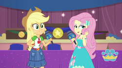 Size: 1920x1080 | Tagged: safe, screencap, applejack, fluttershy, best in show: the victory lap, equestria girls, g4, my little pony equestria girls: better together, applejack's hat, belt, best in show logo, clothes, collar, cowboy hat, denim, denim skirt, dress, duo, duo female, eyeshadow, female, freckles, geode of fauna, geode of super strength, hair, hat, lidded eyes, magical geodes, makeup, microphone, playing with hair, ponytail, shirt, skirt, t-shirt, teenager