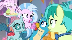 Size: 1280x720 | Tagged: safe, screencap, gallus, ocellus, sandbar, silverstream, smolder, changedling, changeling, classical hippogriff, dragon, griffon, hippogriff, pony, g4, she's all yak, amused, bowtie, chips, claws, confused, cupcake, curved horn, flying, folded wings, food, frown, hand on hip, horn, looking up, male, pointing, raised eyebrow, spread wings, talons, teenager, tray, wings