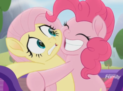 Size: 970x716 | Tagged: safe, screencap, fluttershy, pinkie pie, pony, g4, my little pony: rainbow roadtrip, cropped, discovery family logo, duo, hug, smiling, varying degrees of want