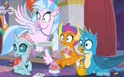Size: 1024x634 | Tagged: safe, screencap, gallus, ocellus, silverstream, smolder, changedling, changeling, classical hippogriff, dragon, griffon, hippogriff, g4, she's all yak, card game, dragoness, eating, female, flying, jewelry, male, necklace, needs more jpeg, plate, playing card, puffy cheeks
