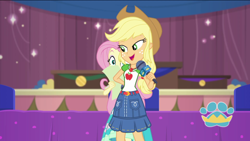 Size: 1920x1080 | Tagged: safe, screencap, applejack, fluttershy, best in show: the pre-show, equestria girls, g4, spoiler:eqg series (season 2), applejack's hat, applejack's shirt with a collar, arm behind back, best in show logo, clothes, collar, collar shirt, cowboy hat, denim skirt, dress, duo, duo female, female, freckles, hair, hat, hiding, looking back, microphone, ponytail, shirt, shirt with a collar, skirt, smiling, t-shirt, teenager