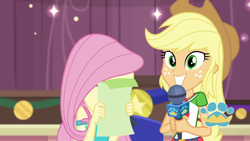 Size: 1920x1080 | Tagged: safe, screencap, applejack, fluttershy, best in show: the pre-show, equestria girls, g4, my little pony equestria girls: better together, applejack's hat, belt, best in show logo, clothes, cowboy hat, cute, cutie mark, cutie mark on clothes, denim skirt, duo, duo female, embarrassed, female, geode of super strength, grin, hat, jackabetes, jewelry, magical geodes, microphone, necklace, shy, skirt, smiling