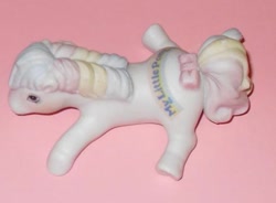 Size: 579x426 | Tagged: safe, photographer:absol, first born, earth pony, pony, g1, adoraborn, bow, cute, female, irl, lying down, mare, multicolored hair, my little pony logo, photo, porcelain, porcelain figurine, prone, rainbow hair, smiling, solo, sploot, tail, tail bow, toy