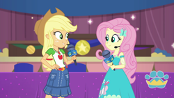 Size: 1000x563 | Tagged: safe, screencap, applejack, fluttershy, best in show: the victory lap, equestria girls, g4, my little pony equestria girls: better together, applejack's hat, clothes, cowboy hat, dress, geode of fauna, geode of super strength, hand on hip, hat, looking at each other, magical geodes, microphone, skirt, smiling