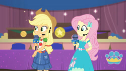 Size: 3410x1920 | Tagged: safe, screencap, applejack, fluttershy, best in show: the victory lap, equestria girls, equestria girls series, g4, spoiler:eqg series (season 2), applejack's hat, belt, best in show logo, clothes, cowboy hat, cutie mark, cutie mark on clothes, denim skirt, female, geode of fauna, geode of super strength, hairpin, hand on hip, hat, jewelry, magical geodes, microphone, necklace, skirt, smiling