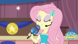 Size: 3410x1920 | Tagged: safe, screencap, fluttershy, best in show: the victory lap, equestria girls, g4, my little pony equestria girls: better together, best in show logo, eyes closed, female, geode of fauna, hairpin, jewelry, magical geodes, microphone, necklace, smiling, solo