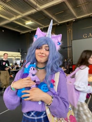 Size: 3024x4032 | Tagged: safe, artist:hysteriana, izzy moonbow, human, pony, unicorn, g5, blue hair, brony, choker, clothes, cosplay, costume, ear fluff, ear piercing, female, festival, hug, irl, irl human, jewelry, nail polish, nails, nature, photo, piercing, plushie, pony plushie, skirt, smiling, solo, sweater, toy