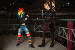 Size: 1280x853 | Tagged: safe, artist:helen the witch, artist:pegasus_fs, rainbow dash, human, g4, armor, boots, clothes, cosplay, costume, glasses, grin, irl, irl human, jacket, leather, leather jacket, looking at each other, looking at someone, photo, rainbow socks, rubronycon, shadowbolts, shadowbolts costume, shoes, smiling, socks, striped socks