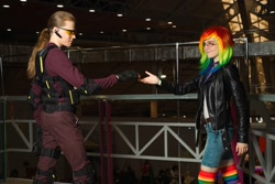 Size: 1280x853 | Tagged: safe, artist:helen the witch, artist:pegasus_fs, rainbow dash, human, g4, armor, clothes, cosplay, costume, glasses, irl, irl human, jacket, leather, leather jacket, looking at each other, looking at someone, photo, rainbow socks, reaching, rubronycon, shadowbolts, shadowbolts costume, smiling, socks, striped socks