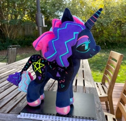 Size: 2048x1962 | Tagged: safe, artist:orky, oc, oc only, oc:twinkle pop, pony, unicorn, black sclera, book, chair, commission, female, horn, irl, leonine tail, lidded eyes, mare, outdoors, photo, plushie, pony plushie, smiling, solo, standing, table, tail, unicorn oc