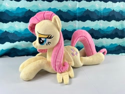Size: 4032x3024 | Tagged: safe, artist:kazzysart, fluttershy, pegasus, pony, g4, female, irl, lidded eyes, lying down, mare, photo, pink mane, pink tail, plushie, prone, solo, tail, wings, yellow coat
