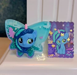 Size: 2841x2785 | Tagged: safe, misty brightdawn, butterfly, pony, g5, official, acrylic plastic, book, card, chibi, dinosaw, front view, indoors, irl, merchandise, opaline's dark castle, photo, shaker, window