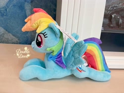 Size: 4062x3046 | Tagged: safe, reesee, rainbow dash, pegasus, pony, g4, official, irl, lying down, merchandise, photo, plushie, pony plushie, side view, smiling, solo, spread wings, text, wings