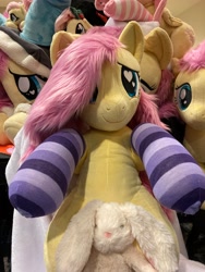 Size: 3024x4032 | Tagged: safe, artist:calusariac, artist:qtpony, fluttershy, pegasus, pony, rabbit, everfree northwest, g4, animal, blanket, clothes, cute, everfree northwest 2024, heart, heart eyes, hoodie, indoors, irl, multeity, photo, plushie, shyabetes, smiling, socks, striped socks, wingding eyes