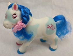 Size: 2560x1953 | Tagged: safe, earth pony, pony, bootleg, bow, braid, coat markings, colored hooves, curly hair, cute, facial markings, female, filly, foal, hair bow, lanard, party ponies, photo, pinto, smiling, solo, star (coat marking), toy, unshorn fetlocks