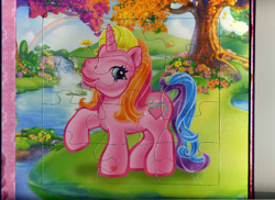 Size: 800x581 | Tagged: safe, egmont, rarity (g3), pony, unicorn, g3, official, 2d, book, flower, horn, jigsaw puzzle, lake, looking at you, puzzle, rainbow, raised hoof, scan, smiling, smiling at you, standing, tree, water
