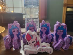 Size: 4032x3024 | Tagged: safe, izzy moonbow, zipp storm, pegasus, pony, unicorn, g5, eraser, female, horn, irl, lying down, meme, merchandise, photo, piper perri surrounded, plate, prone, surrounded, table, water bottle