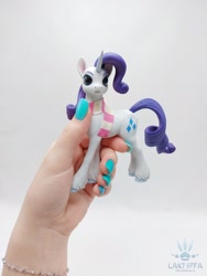 Size: 1620x2160 | Tagged: safe, alternate angle, alternate version, artist:lakterra, rarity, human, pony, unicorn, g4, clothes, craft, female, figurine, hand, holding a pony, horn, irl, mare, photo, polymer clay, scarf, signature, simple background, striped scarf, tail, unshorn fetlocks, white background