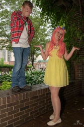 Size: 684x1024 | Tagged: safe, big macintosh, fluttershy, human, g4, 2015, brick wall, clothes, cosplay, costume, cutie mark on clothes, denim, dress, duo, duo male and female, facepalm, female, floral head wreath, flower, holding hands, irl, irl human, jeans, male, outdoors, pants, photo, plaid shirt, ship:fluttermac, shipping, shirt, shoes, shrug, straight, t-shirt, tree, wig, wings