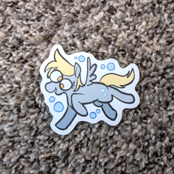 Size: 971x971 | Tagged: safe, artist:punkittdev, derpy hooves, pegasus, pony, g4, blonde mane, blonde tail, bubble, carpet, colored, derp, eye clipping through hair, eyelashes, female, flat colors, gray coat, irl, mare, no catchlights, no pupils, open mouth, open smile, photo, raised hoof, raised leg, running, small wings, smiling, solo, spread wings, sticker, sticker design, tail, wings